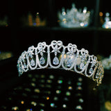  sparkling silver tiara featuring intricate heart-shaped designs and dangling teardrop zirconia stones. The large zirconia stones are suspended to create a dynamic, shimmering effect.